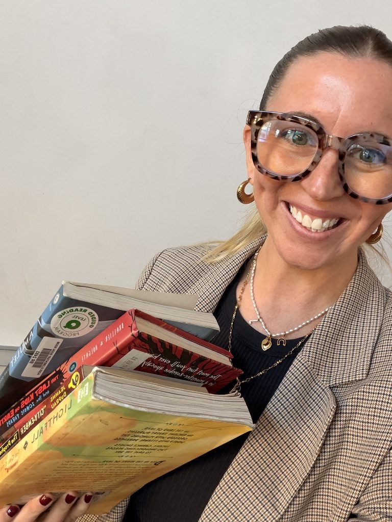 Dr. Jenn Overstreet smiling, holding a stack of chapter books
